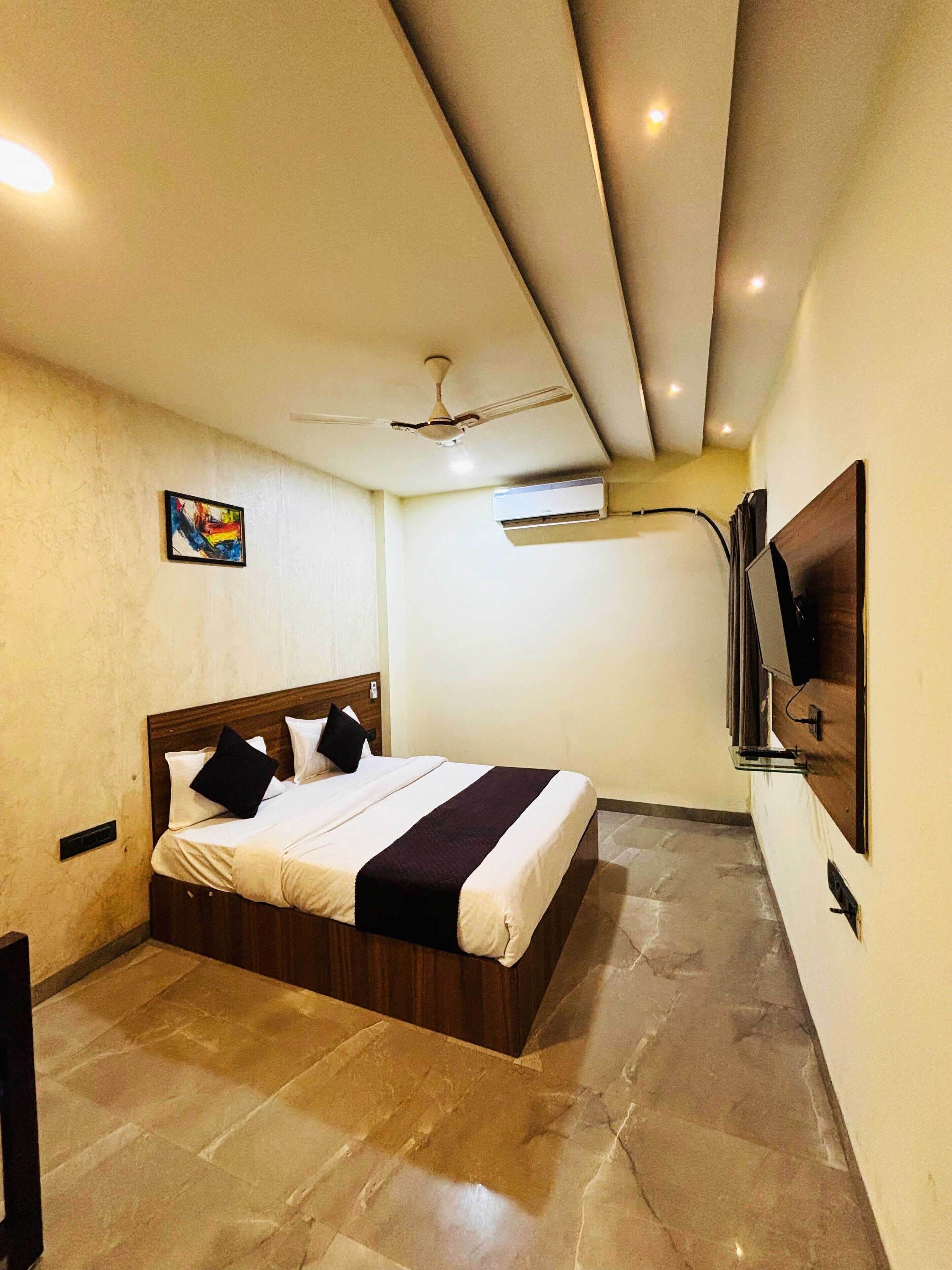 A bedroom with a bed, a ceiling fan, an air conditioning unit, and a mounted television.
