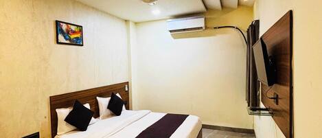 A bedroom with a bed, a ceiling fan, an air conditioning unit, and a mounted television.