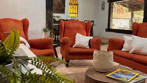 A cozy living room with two orange armchairs, a wooden coffee table with a magazine, and a large window with a view of the outdoors.