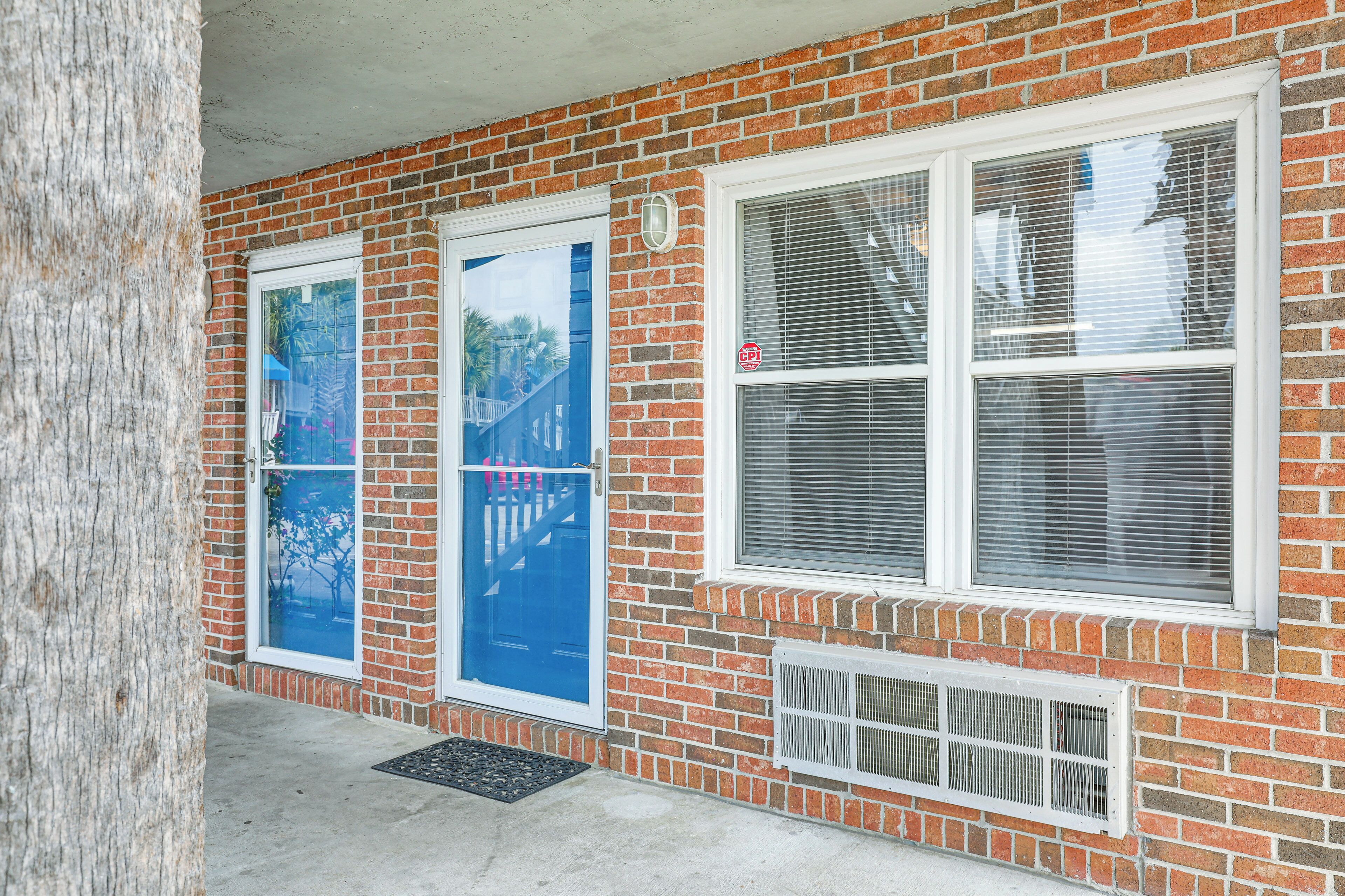 A brick building with two windows, one with a blue door and another with a white door.