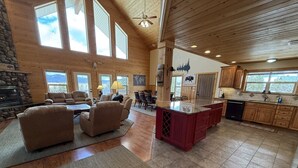 A spacious living area with a fireplace, large windows, and a kitchen with wooden cabinets.