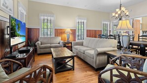 A spacious living room with a large flat-screen TV, two sofas, a coffee table, and a dining area with a chandelier. - Southern Pines- Sleeps 20 with community pool and docks (Steinhatchee)