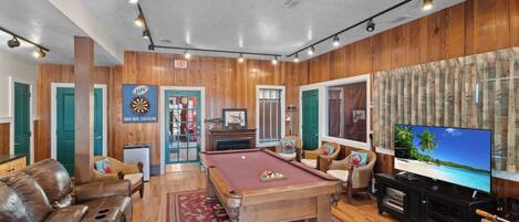 A pool table in a room with wooden walls, a television, and a sofa.