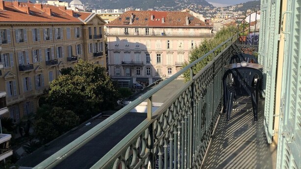 A balcony with a view of a cityscape, including buildings and a hill in the distance.