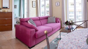 A living room with a pink sofa, a wooden dresser, and a dining table with a floral table runner.