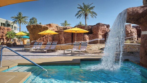 A pool area with lounge chairs, umbrellas, and a waterfall feature.