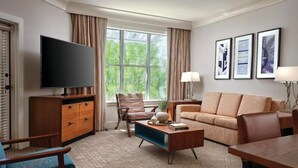 A modern living room with a flat-screen TV, a sofa, a coffee table, and a chair. There are framed pictures on the wall and a window with curtains.
