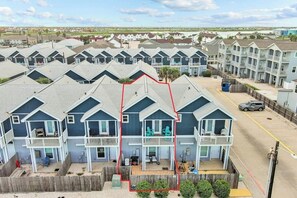 Una hilera de condominios frente al mar de dos pisos, con balcones, una valla de madera y una vista despejada del océano.