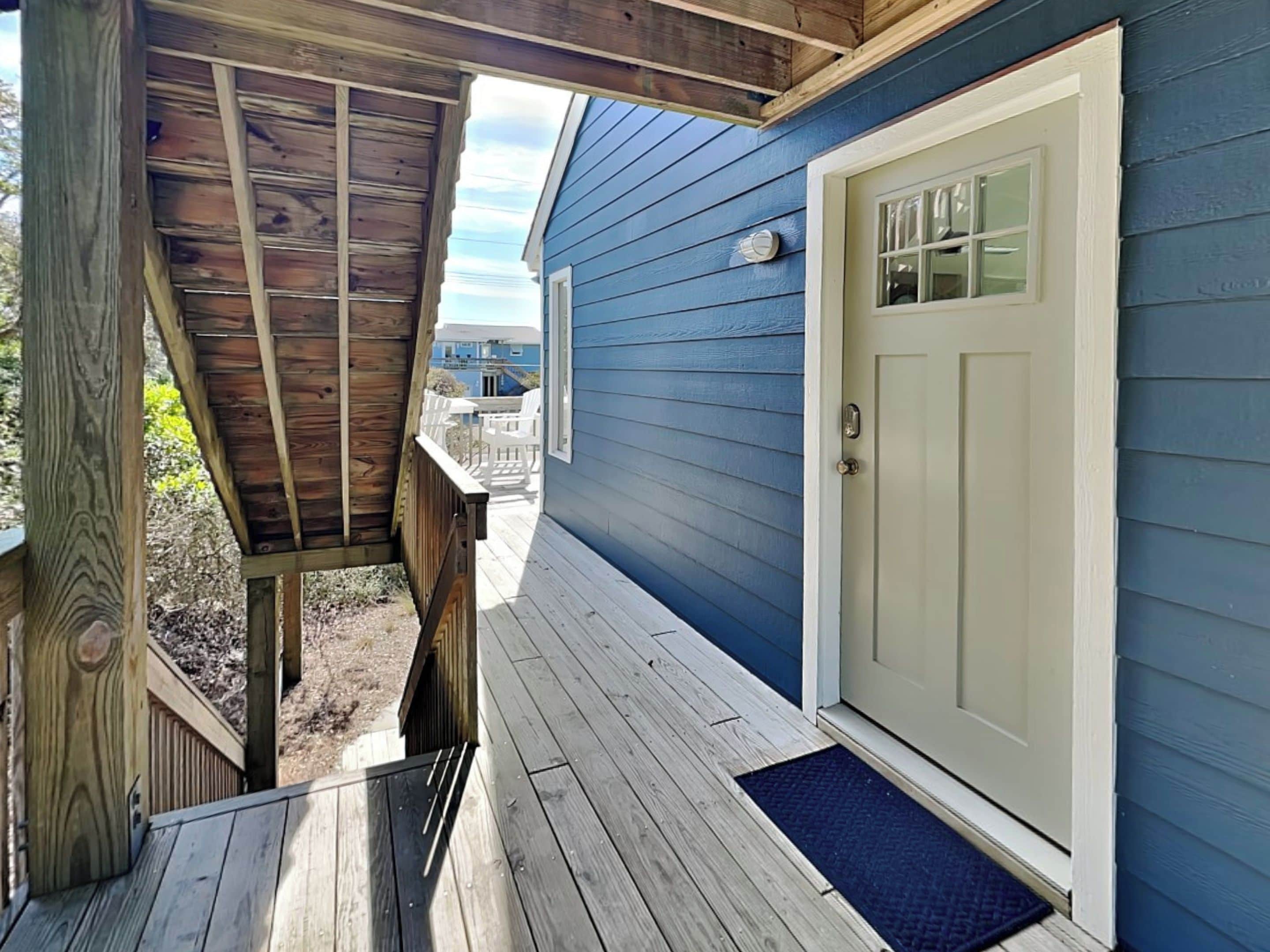 Una terraza de madera que conduce a una casa azul con una puerta blanca y un pequeño porche.
