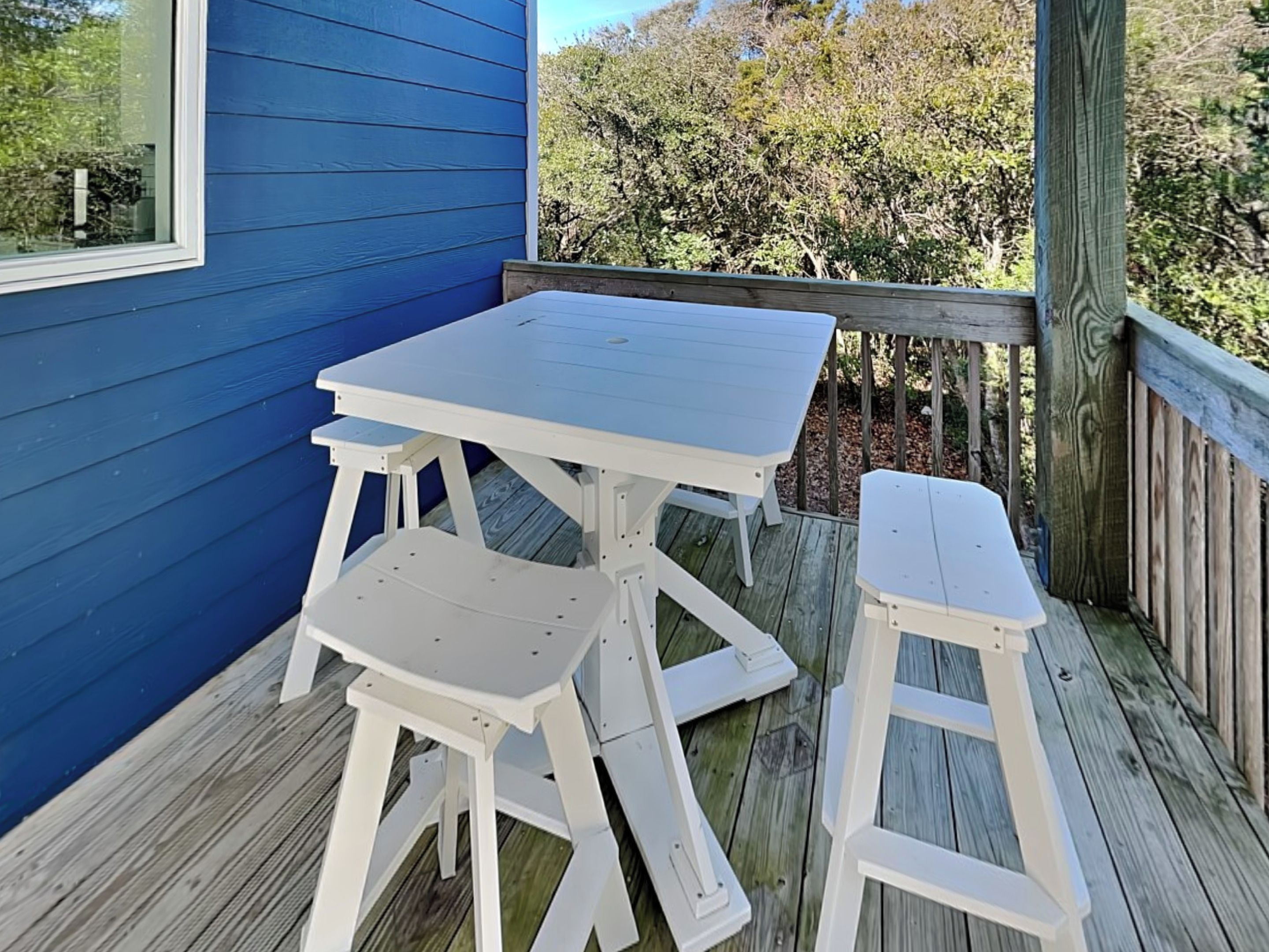 Un edificio azul con una terraza de madera, una mesa blanca y dos bancos blancos.