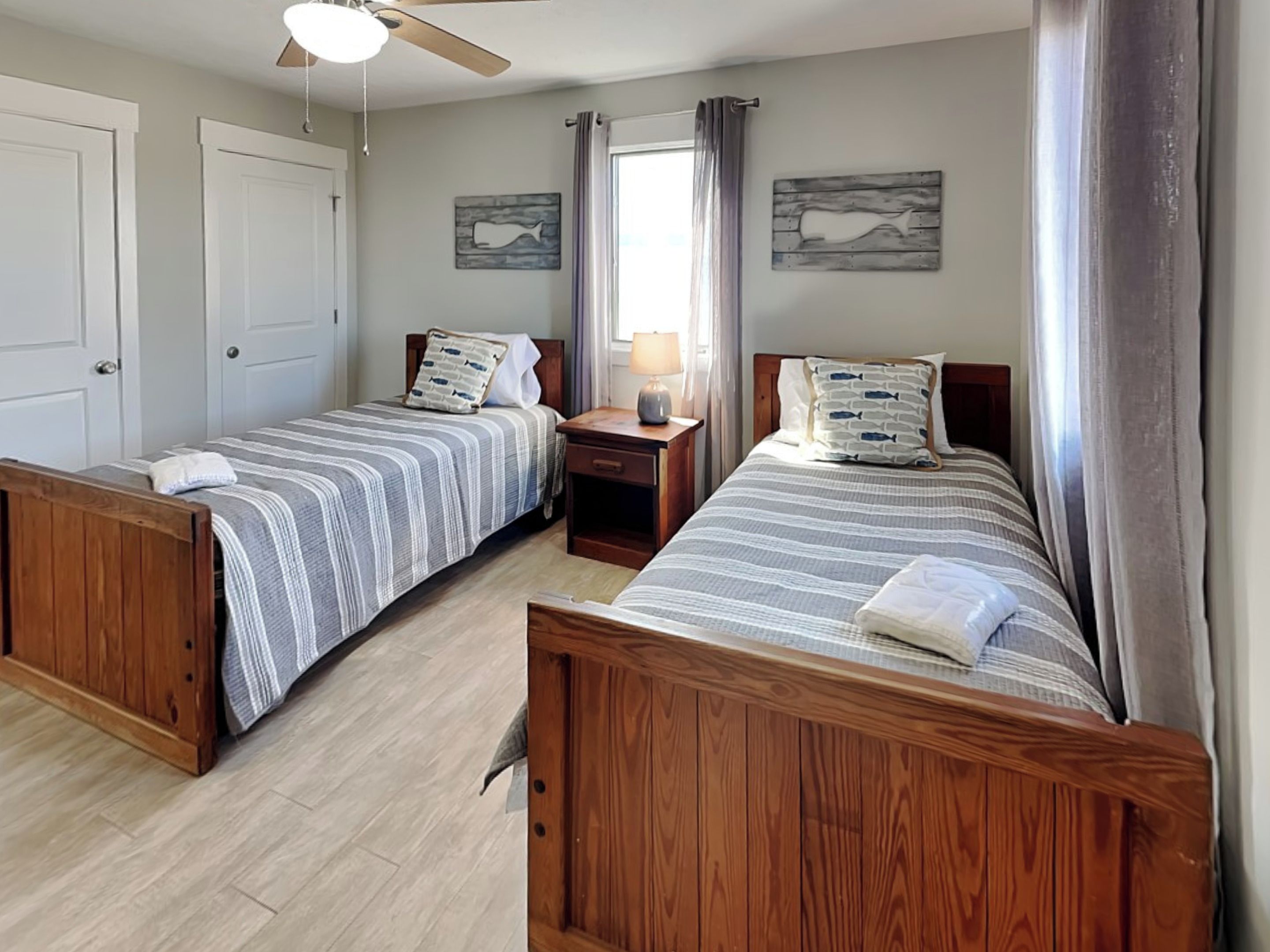 A bedroom with two wooden beds, a nightstand, a ceiling fan, and two wall-mounted artwork pieces.