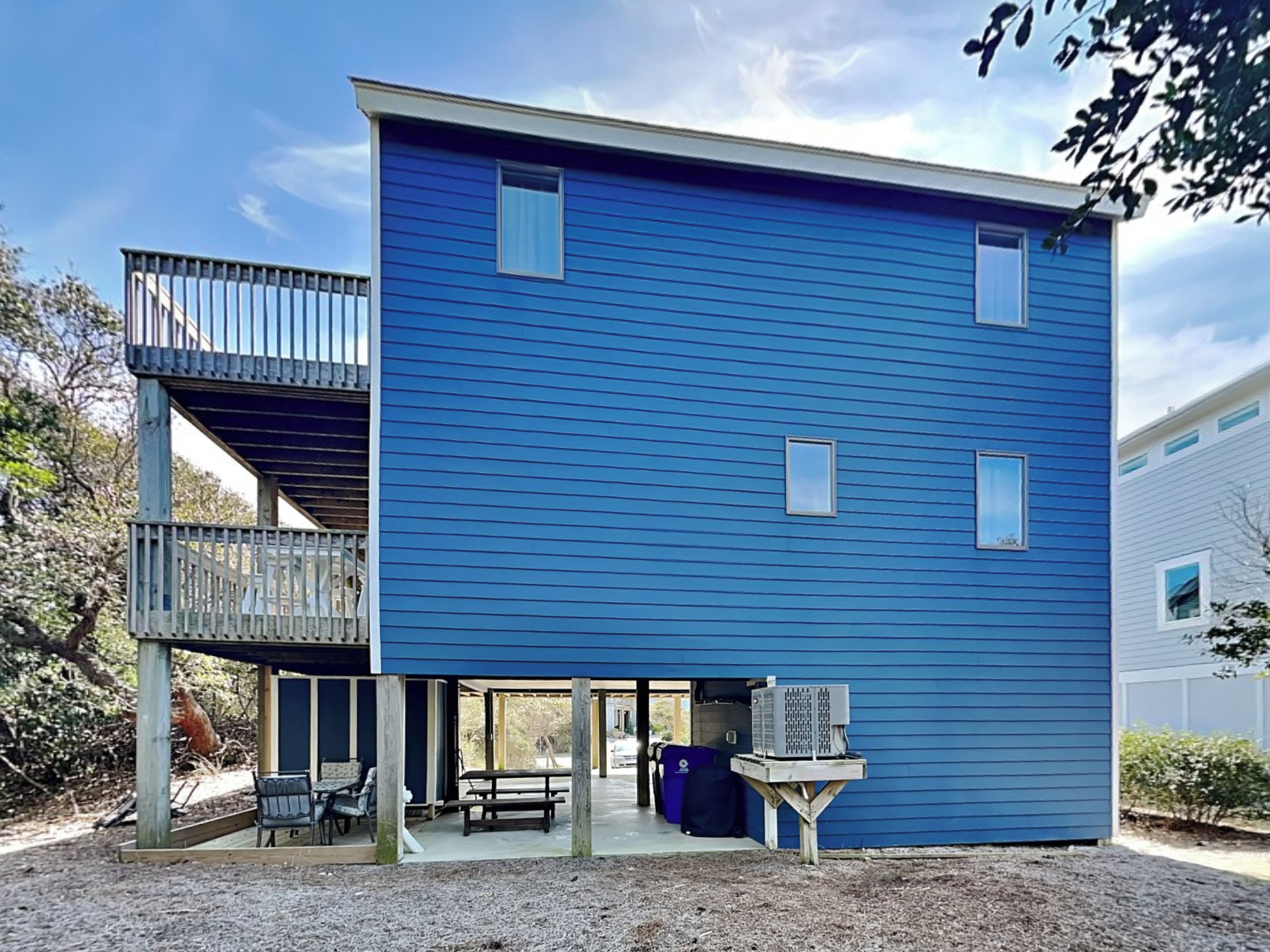 A two-story building with a blue exterior, a covered outdoor seating area, and a small table with a grill.