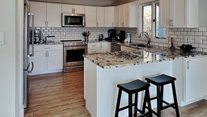 A modern kitchen with white cabinets, a stainless steel oven, a microwave, and a large island with two stools. - Southwind by Topsail Realty (Holly Ridge)
