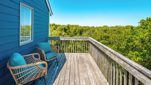 A wooden deck with wicker chairs and a view of dense greenery. - Southwind by Topsail Realty (Holly Ridge)