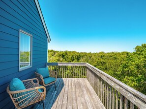 A wooden deck with wicker chairs and a view of dense greenery. - Southwind by Topsail Realty (Holly Ridge)