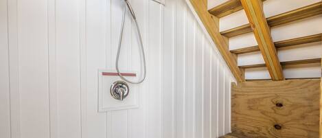 A wooden bench under a sloped ceiling with a showerhead mounted on a white wall.
