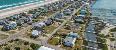 An aerial view of a coastal residential area with houses, a beach, and a pier.
