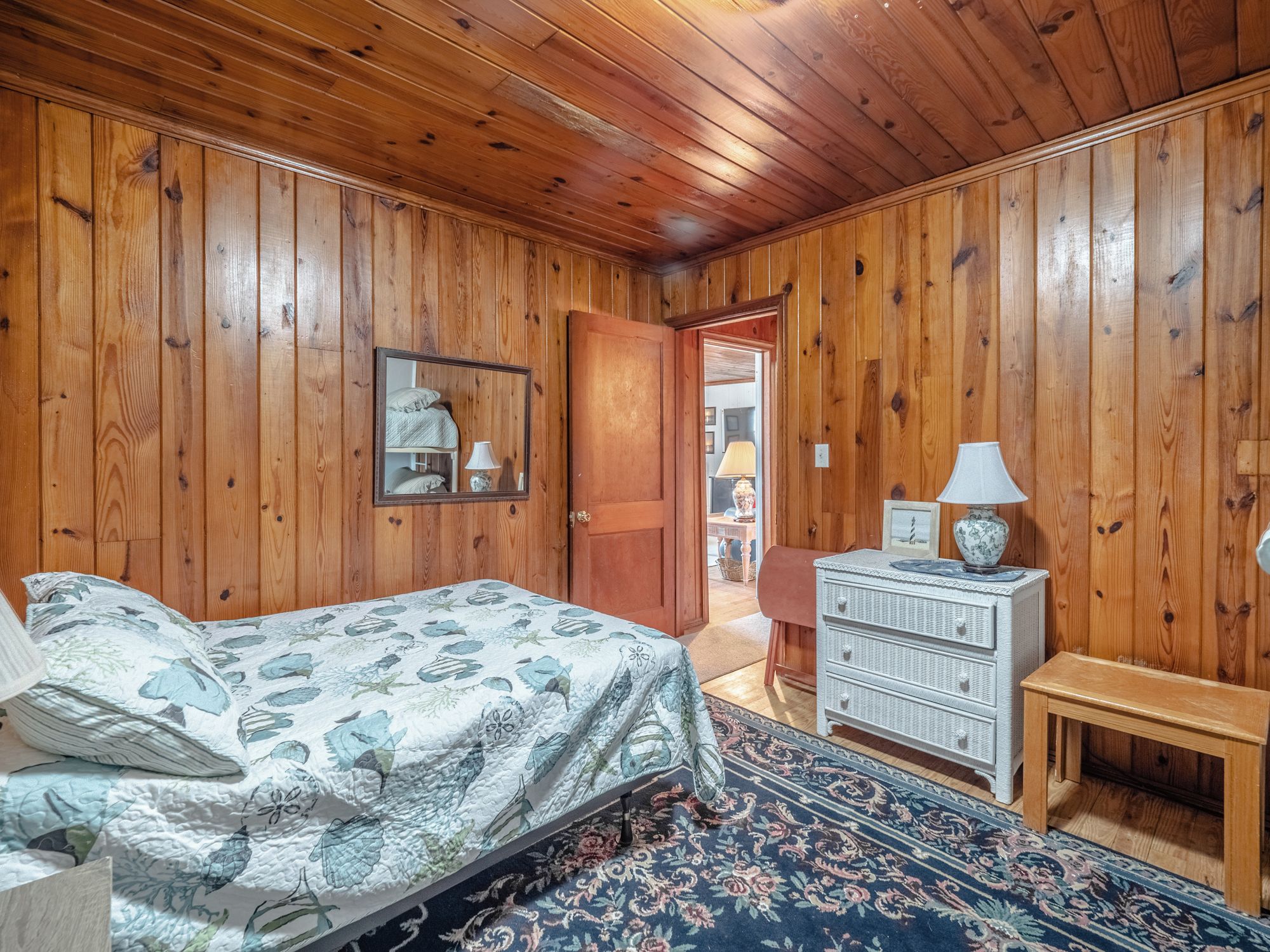 A bedroom with wooden walls, a bed with floral bedding, a dresser, and a mirror.