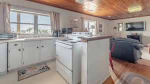 Une cuisine avec des meubles blancs, une cuisinière, un four à micro-ondes et une grande fenêtre.