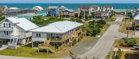A coastal residential area with houses featuring balconies and wooden decks, a road curving through the neighborhood, and the ocean in the background.