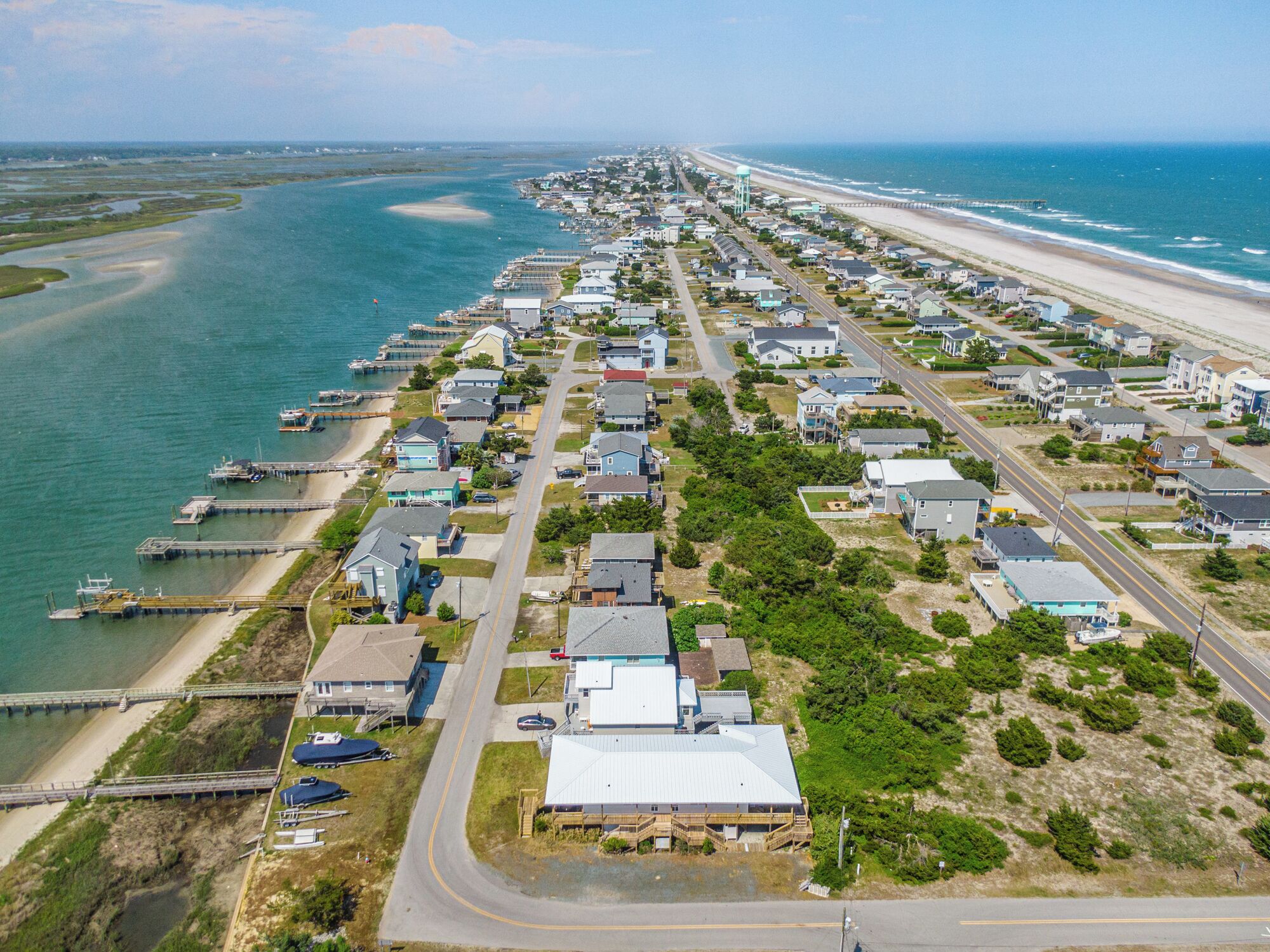 Vue aérienne d’une zone résidentielle côtière, avec des maisons, une plage et une jetée.
