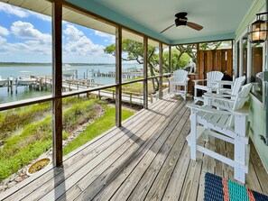 Una terraza de madera con sillas Adirondack blancas que da vista a un puerto deportivo con barcos.