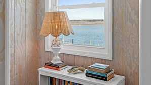 Ein Fenster mit Blick auf ein Gewässer, eine Lampe und ein kleines Regal mit Büchern und einer Dekoration.