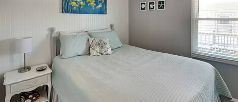 A bedroom with a bed, nightstand, and a window with blinds.