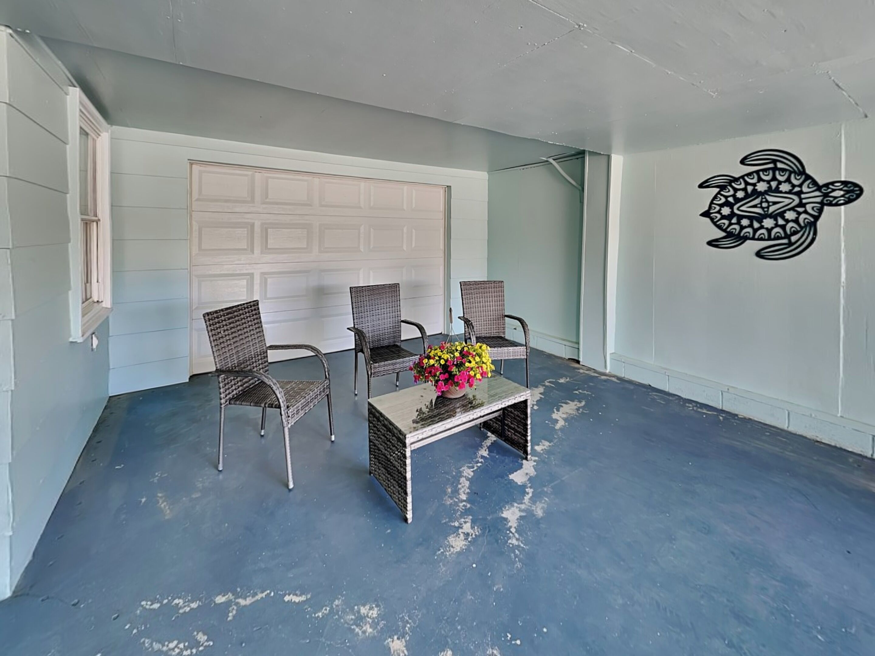A room with two wicker chairs, a coffee table with a floral arrangement, and a white garage door in the background.