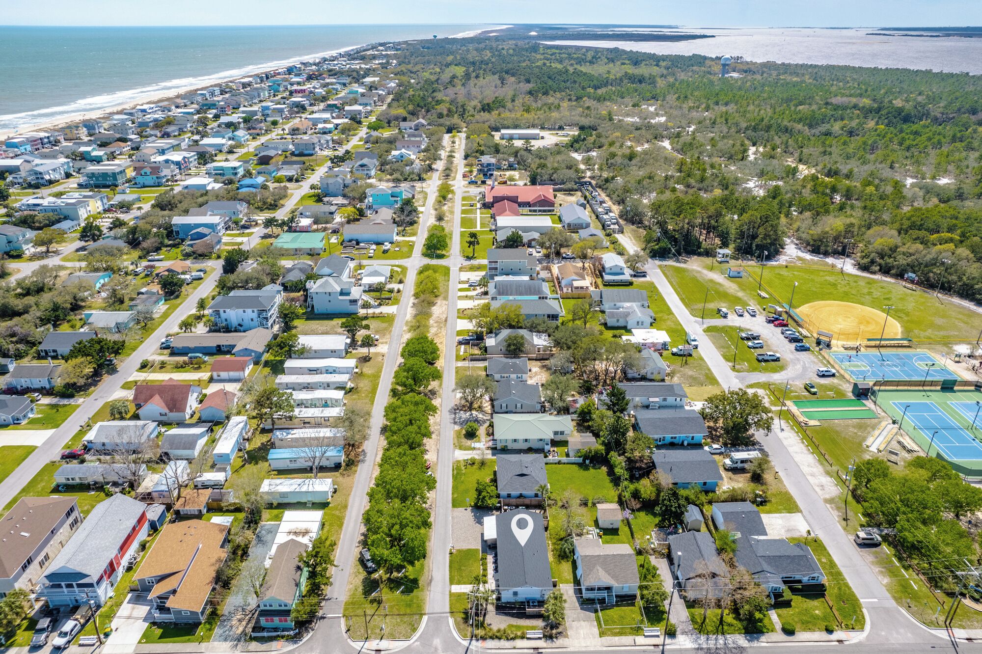 A residential area with houses, a road, and a beach in the background.