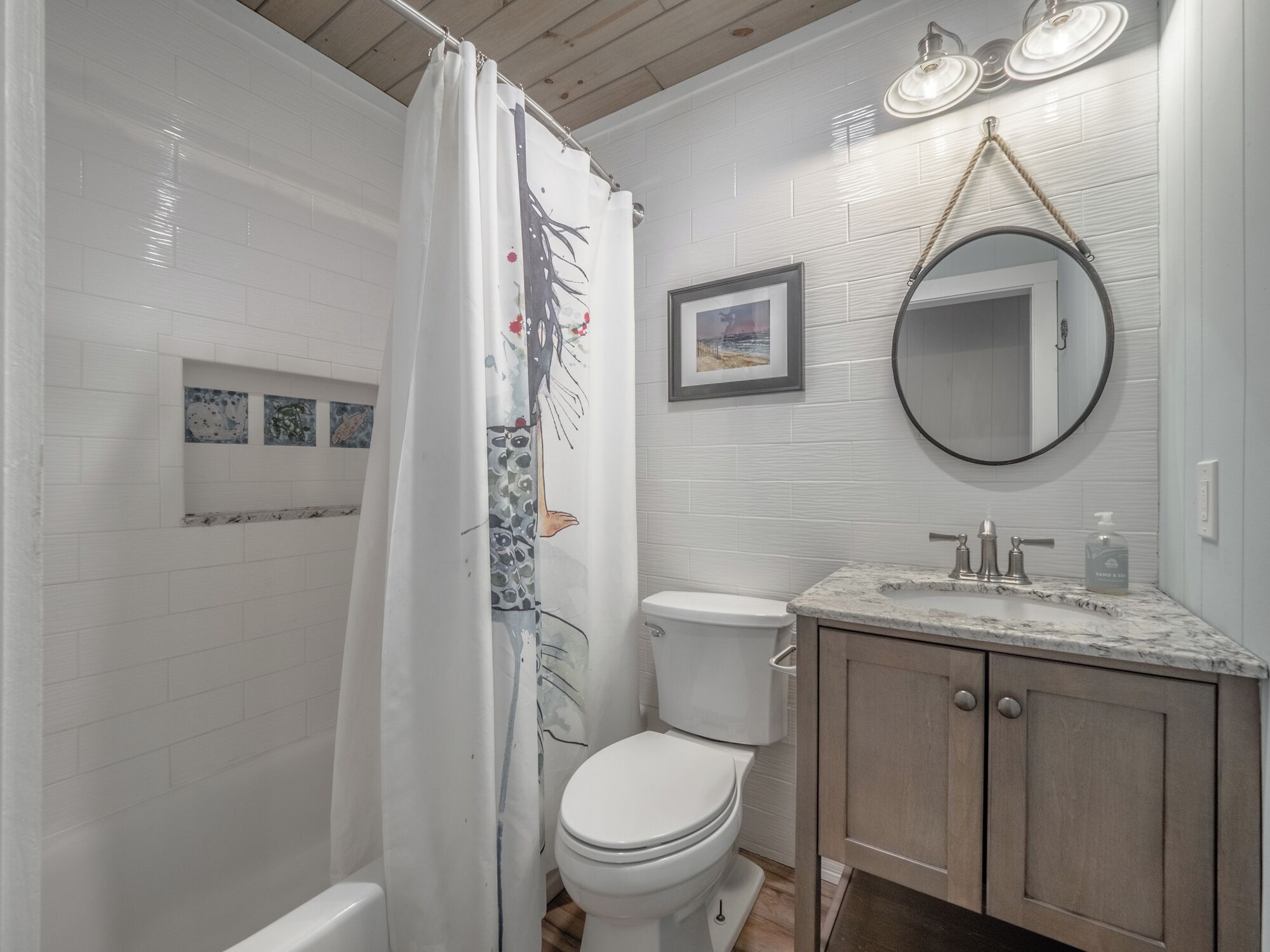 Une salle de bain avec un rideau de douche, des toilettes, un lavabo avec un plan de travail en marbre, des meubles en bois et un miroir.