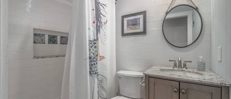 Une salle de bain avec un rideau de douche, des toilettes, un lavabo avec un plan de travail en marbre, des meubles en bois et un miroir.