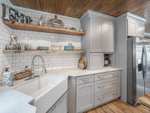 Una cocina moderna con armarios blancos, estantes de madera y un refrigerador de acero inoxidable.