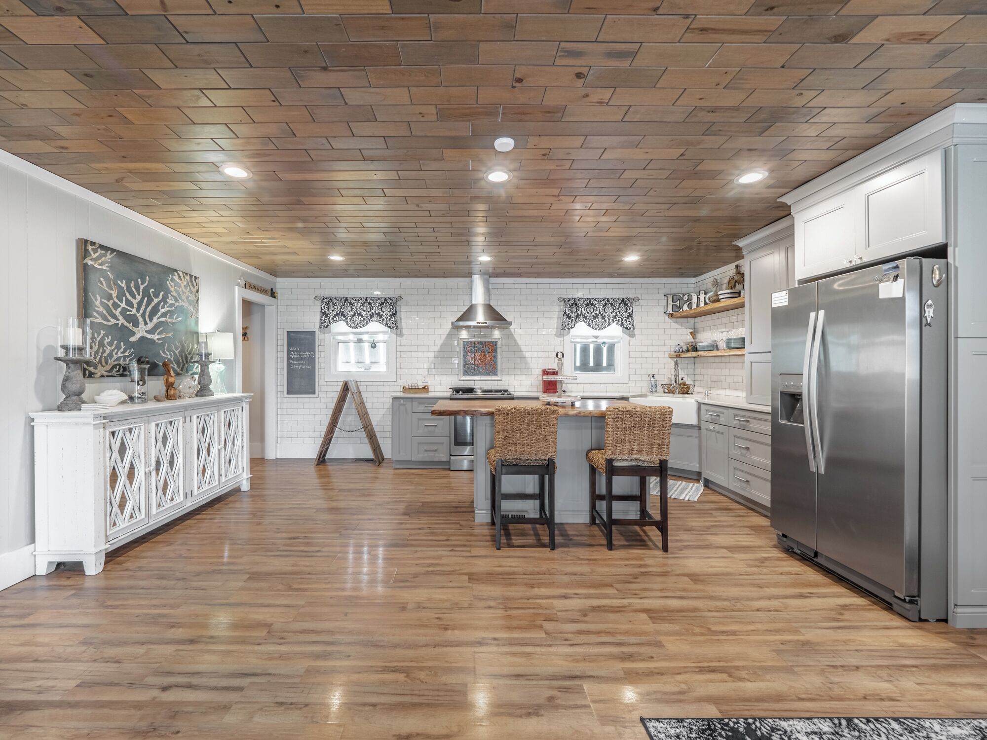 Une cuisine moderne avec un plafond en bois, des meubles blancs et un réfrigérateur en acier inoxydable.