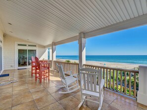 A covered patio with a view of the beach, featuring rocking chairs and a table. - Coppertop by Topsail Realty (Sneads Ferry)