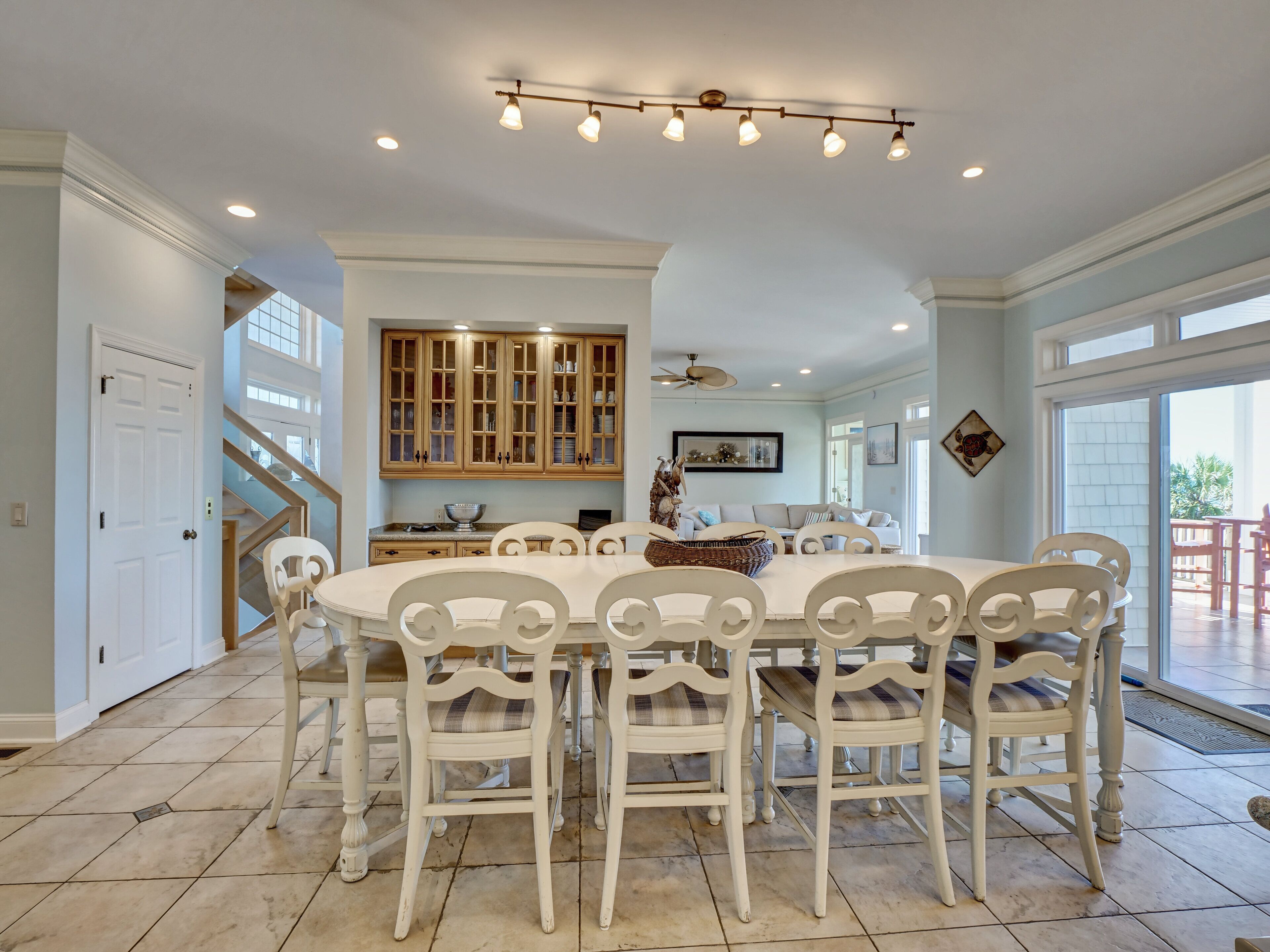 A dining area with a white table and chairs, a kitchen with wooden cabinets, and a staircase.