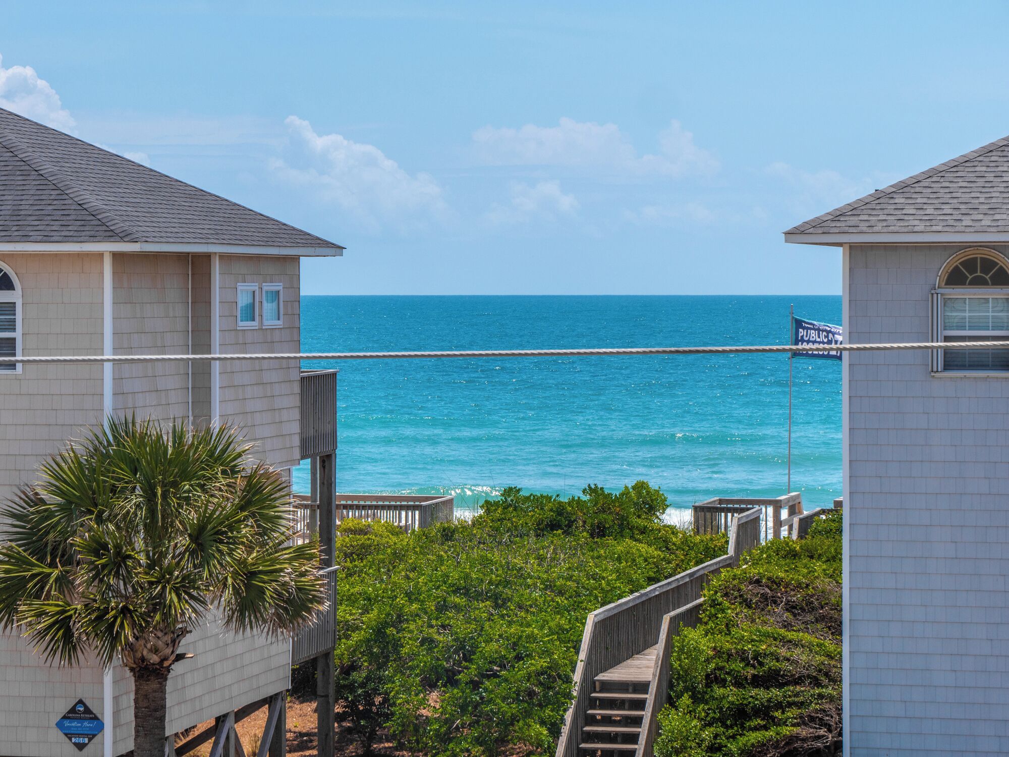 A coastal view with a wooden pier extending into the ocean, surrounded by lush greenery and a clear sky.