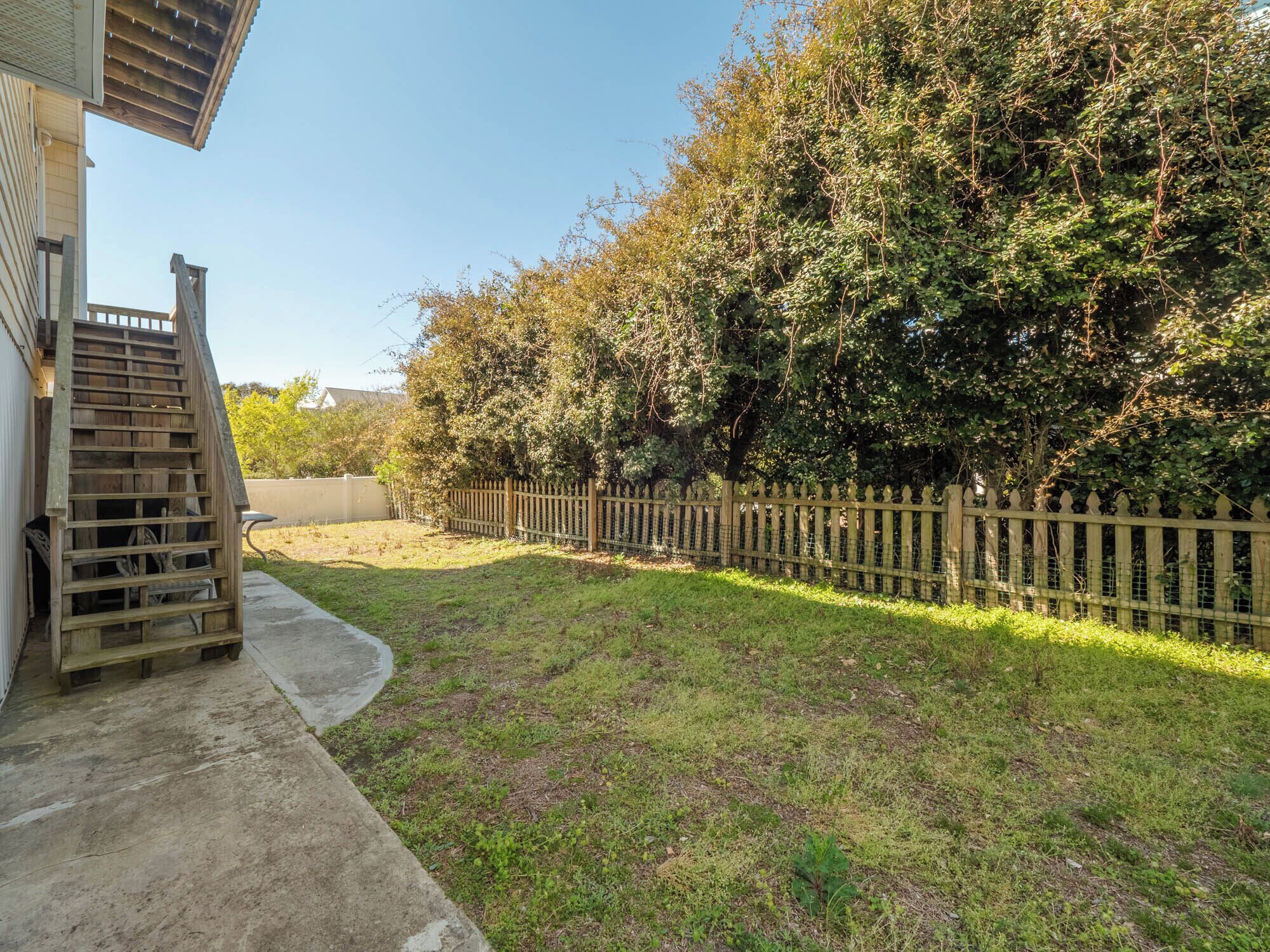 A backyard with a wooden fence, a concrete path, and a grassy area.