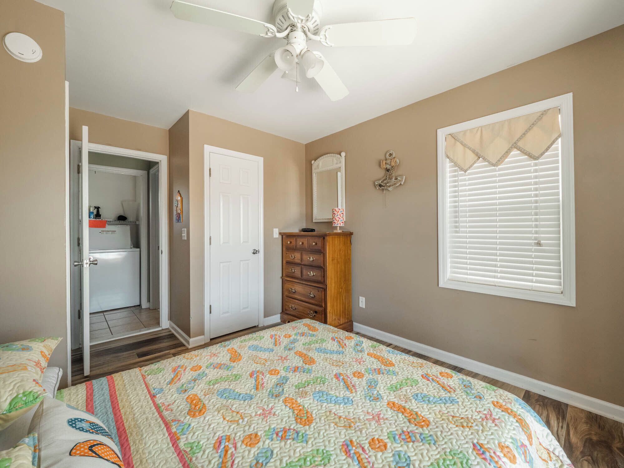 A bedroom with a bed, a dresser, a door, a ceiling fan, and a window with blinds.
