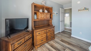 A living room with a wooden entertainment center, a flat-screen TV, and a hallway leading to another room. - Perfectly Tangy by Topsail Realty (Holly Ridge)
