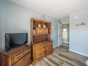 Un salon avec un meuble de rangement en bois pour les appareils multimédias, un téléviseur à écran plat et un couloir menant à une autre pièce.