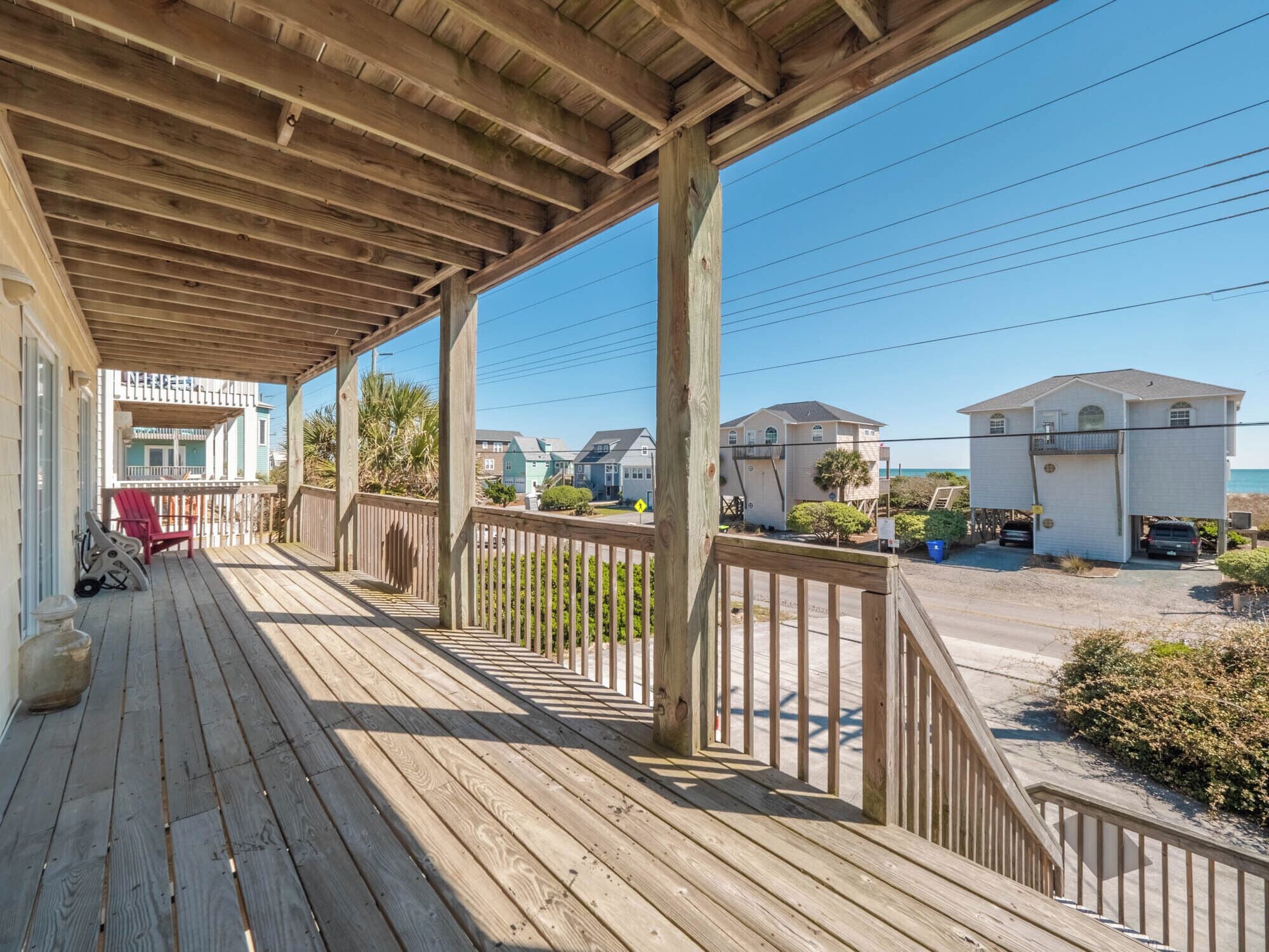 A wooden deck with a railing, overlooking a beach and houses.