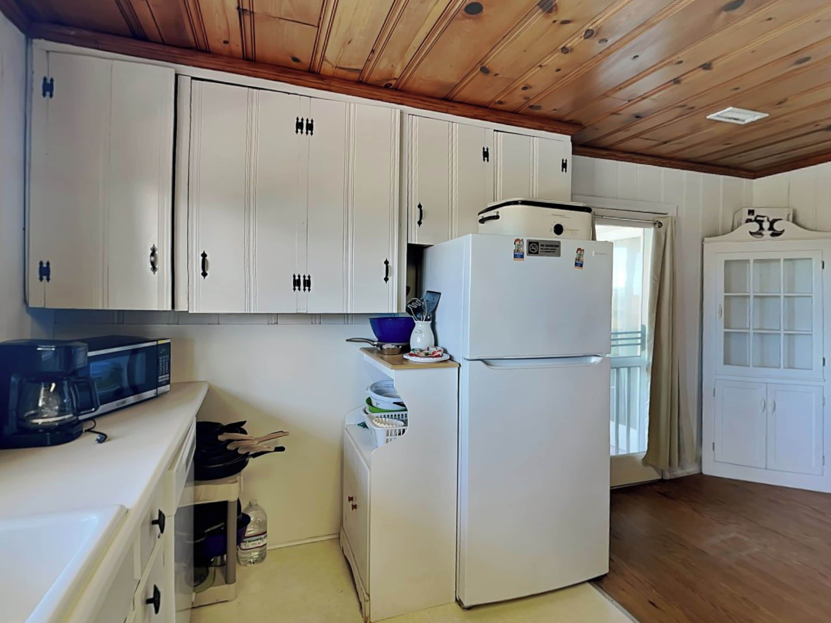 A compact kitchen with white cabinets, a microwave, a refrigerator, and a sink.