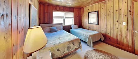 A wooden cabin bedroom with two beds, a nightstand, and a window with blinds.