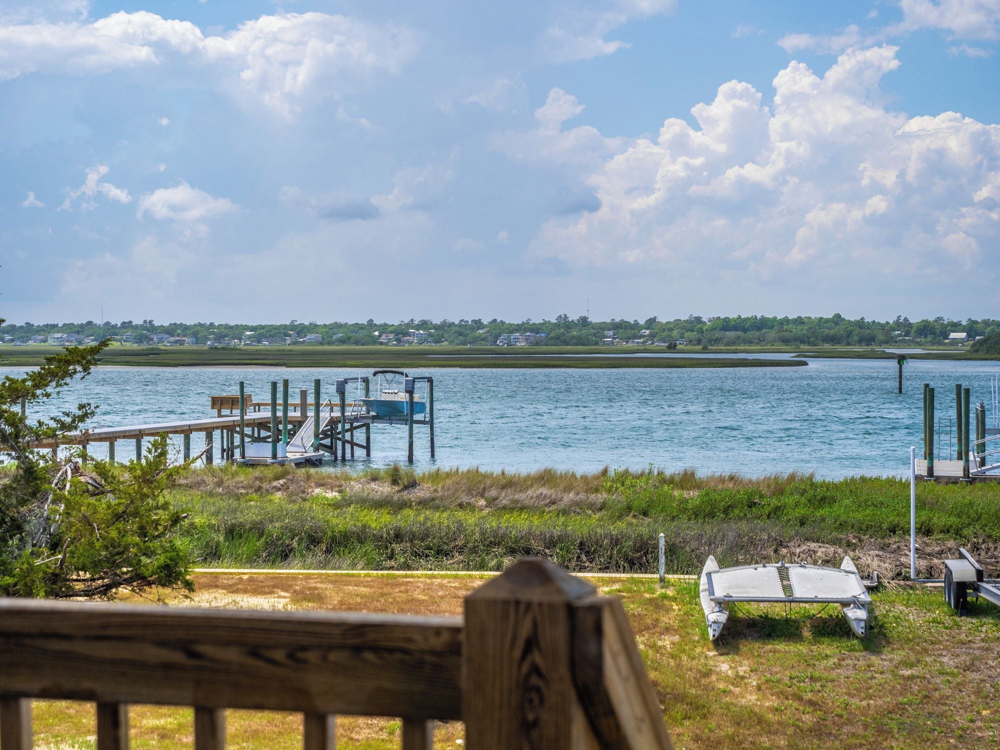A lakeside dock with a boat, a small boat ramp, and a grassy area with a bench.