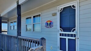 Een huis met een veranda, een blauwe deur en een zonsondergang logo op de muur.