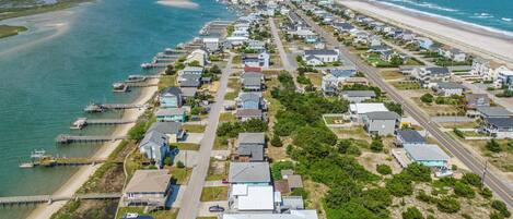 An aerial view of a coastal residential area with houses, a beach, and a pier.