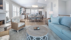 A spacious living room with a blue sofa, a round coffee table, and wicker chairs. - Serenity By the Sea by Carolina Retreats (Kure Beach)