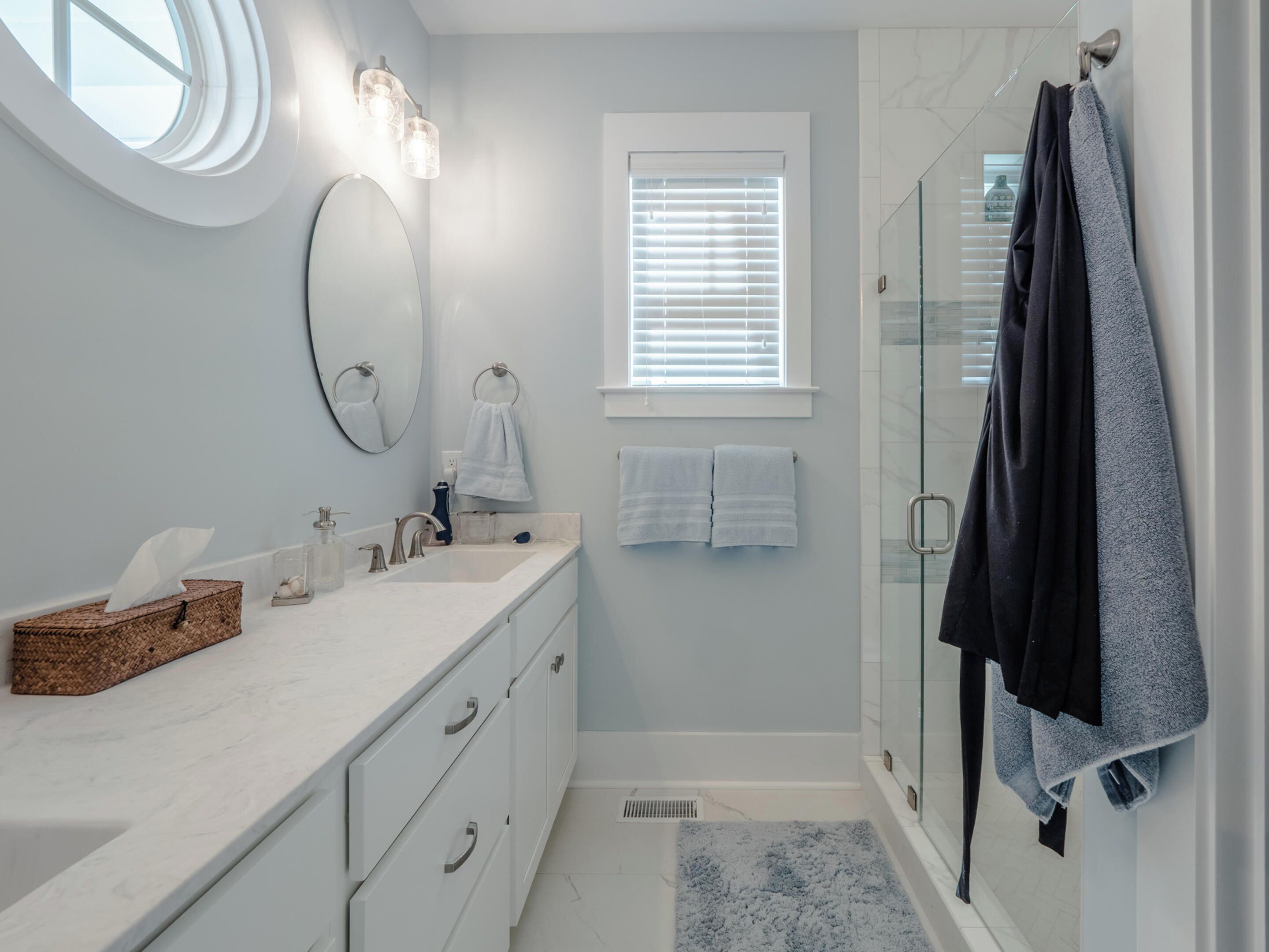 A modern bathroom with a vanity, a glass shower enclosure, and a window with blinds.
