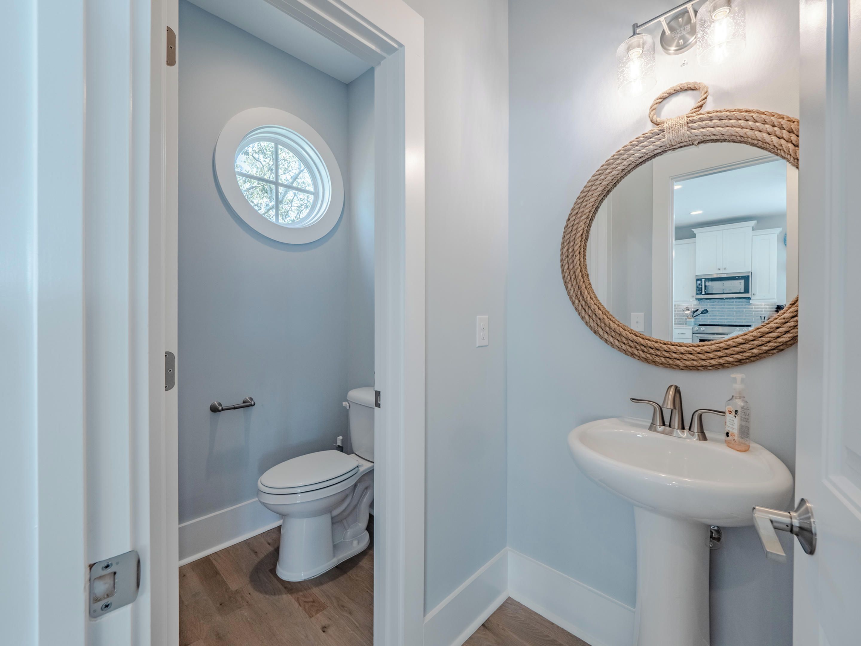 A bathroom with a toilet, a round mirror with a rope frame, and a sink.